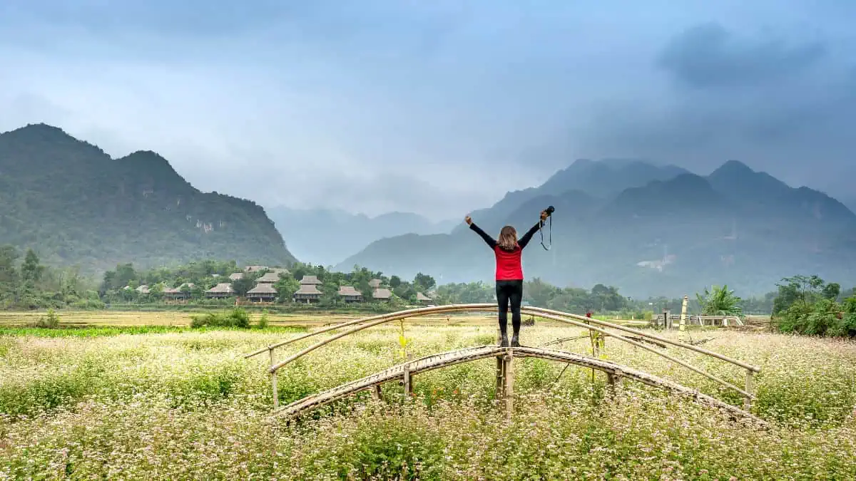 A woman raising both her hands in a field with mountains at the background signifying journey and personal growth