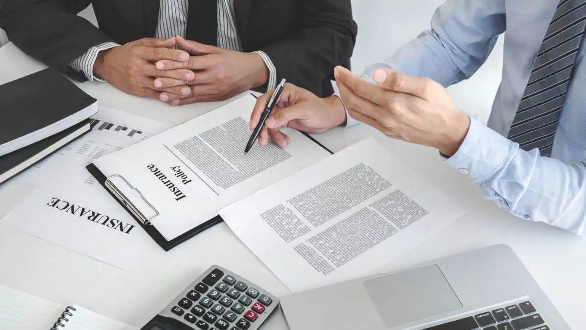 A photo of two men discussing insurance with insurance related document scattered on the table